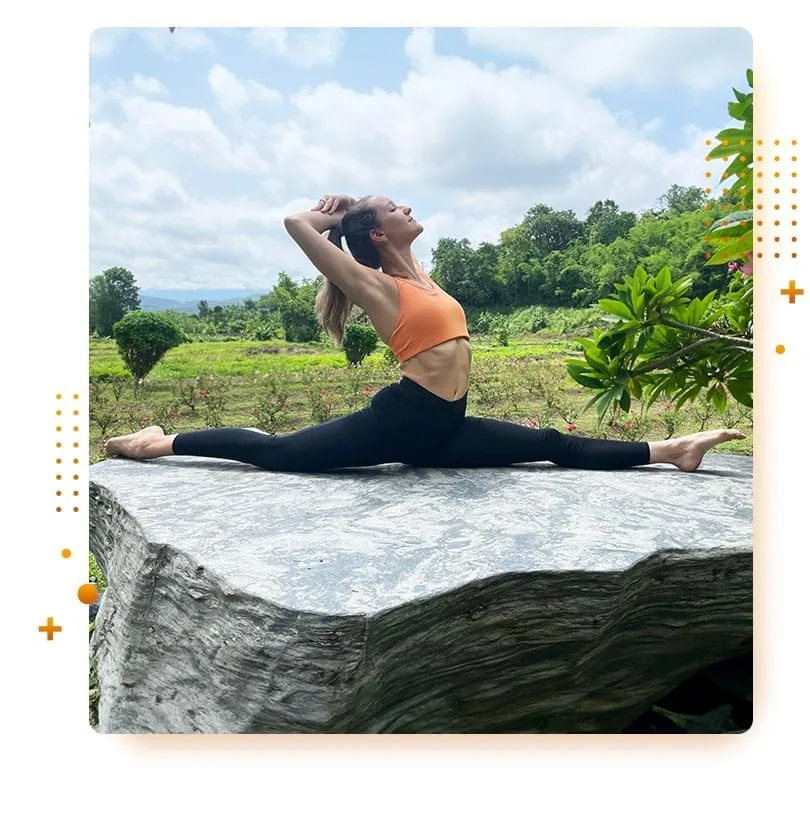 Hanna demonstrating a full split stretch with a backbend outdoors on a large rock, showcasing her flexibility amidst a natural, scenic landscape.